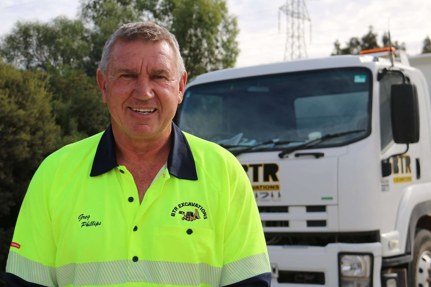 A man in a fluoro shirt in front of a truck