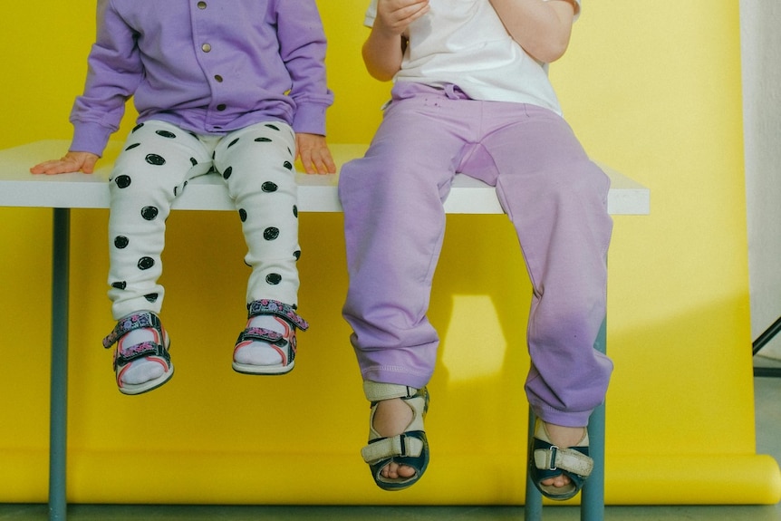 Close-up of two kids wearing purple and white clothes and sitting on table.