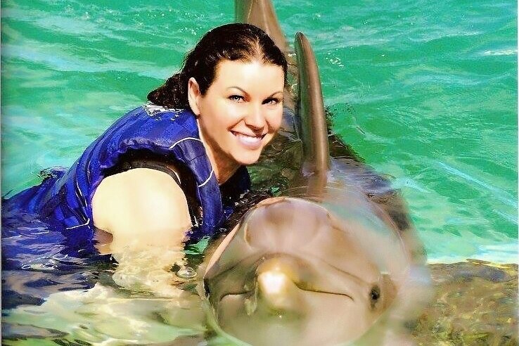A woman smiles as she poses in the water with a dolphin.