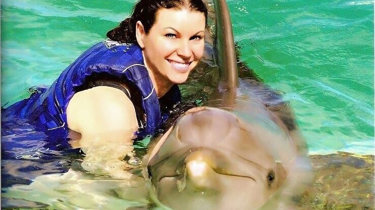 A woman smiles as she poses in the water with a dolphin.