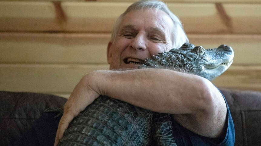 A man hugs a small alligator to his chest