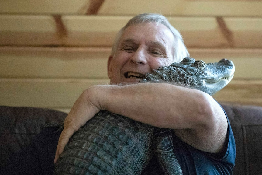 A man hugs a small alligator to his chest