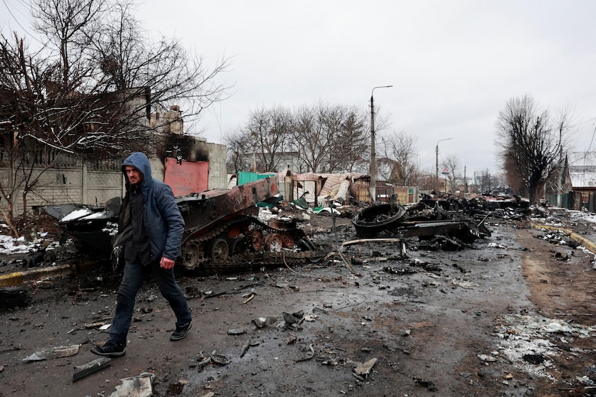A man walks down a street that is covered in burned debris