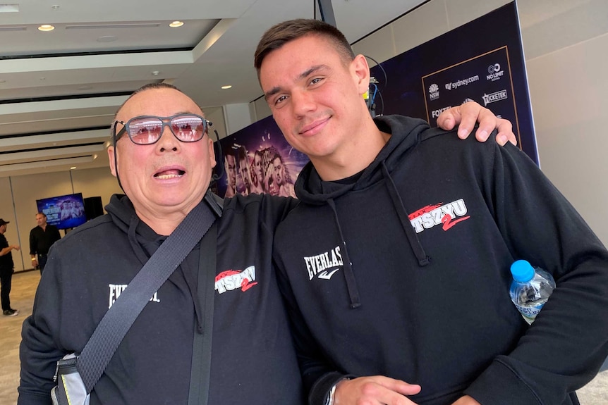 Boris Tszyu stands to the left of his grandson Tim and places his arm around him. They're wearing matching hoodies.