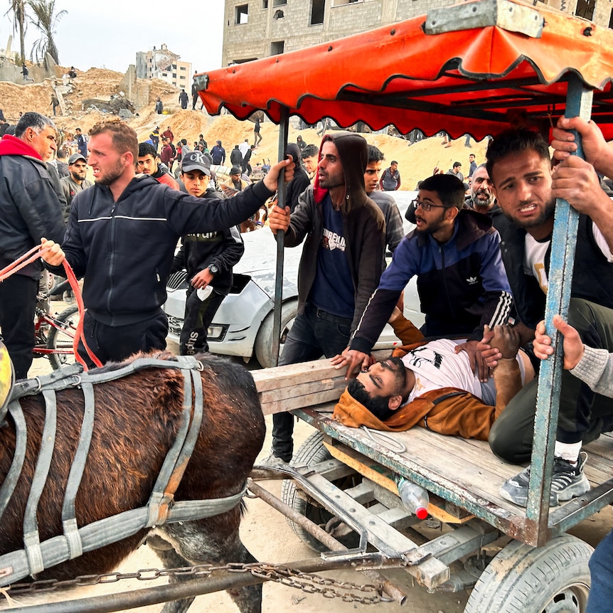 A wounded Palestinian man lies on a cart as Palestinians gather to wait for trucks carrying bags of flour to arrive.