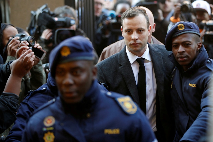 Oscar Pistorius in a suit and tie is escorted by police through media outside a court