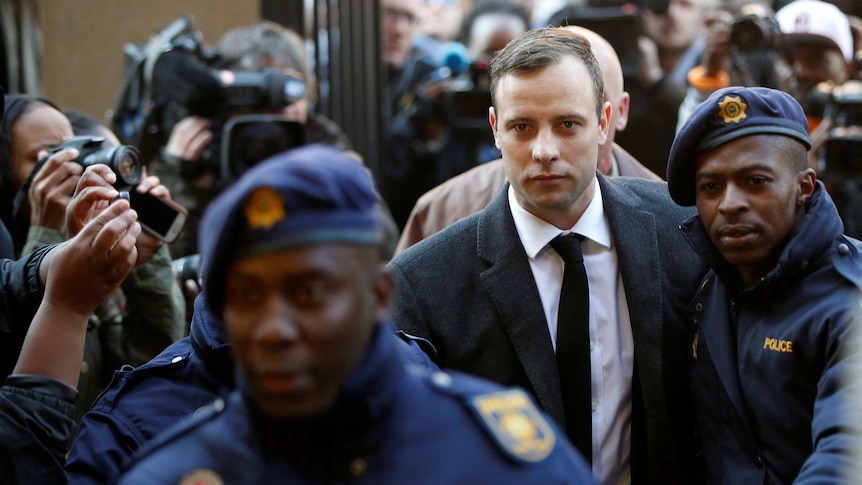 Oscar Pistorius in a suit and tie is escorted by police through media outside a court