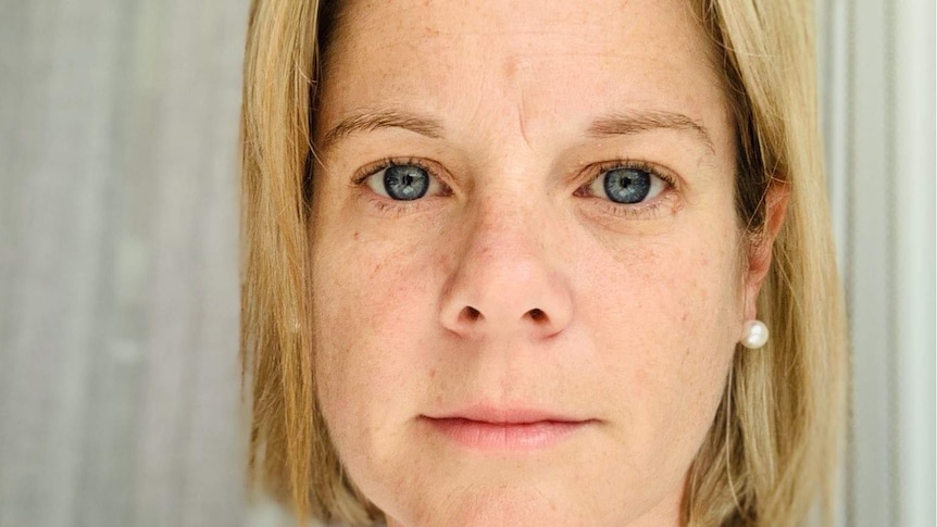 A woman with short blonde hair looks into the camera with a serious expression