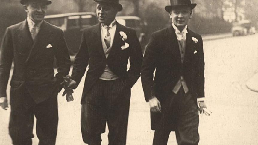 A black and white photograph of three men in suits with top hats, dressed for a wedding. 