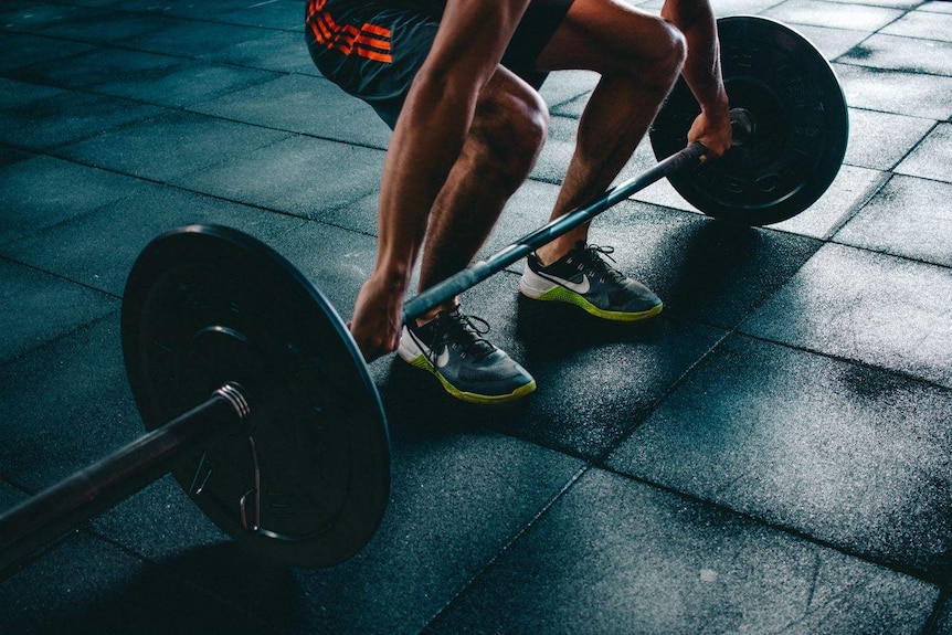 A dark shadowy image of a man lifting weights at the gym.