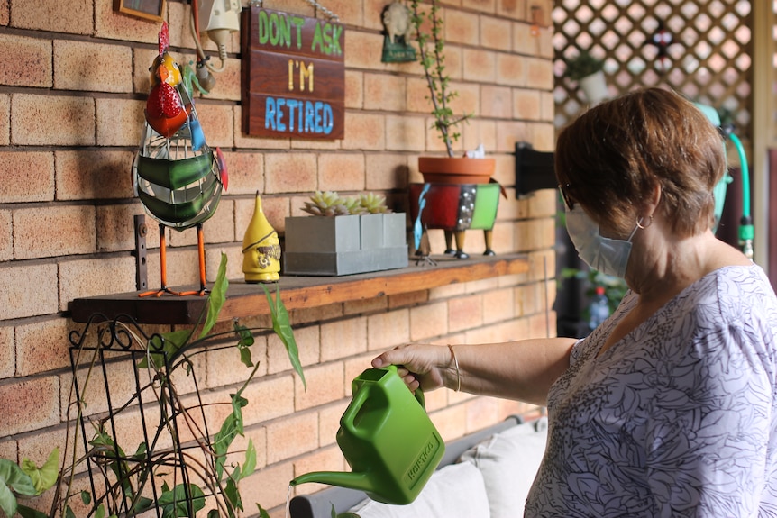 Louise watering plant with green watering can in back courtyard of her home