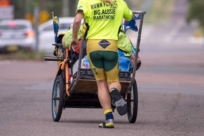 Man runs in thongs and socks pushing a trolley loaded with plastic containers