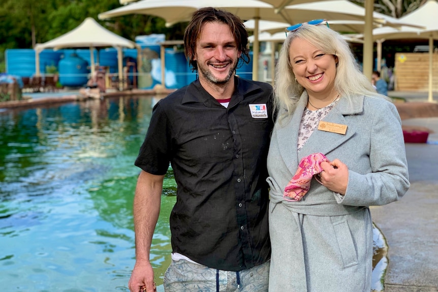 A man and a woman smiling at camera with pool in the background