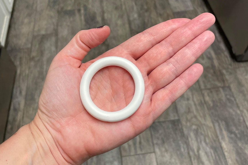 A wide white vaginal ring in the middle of an open left hand