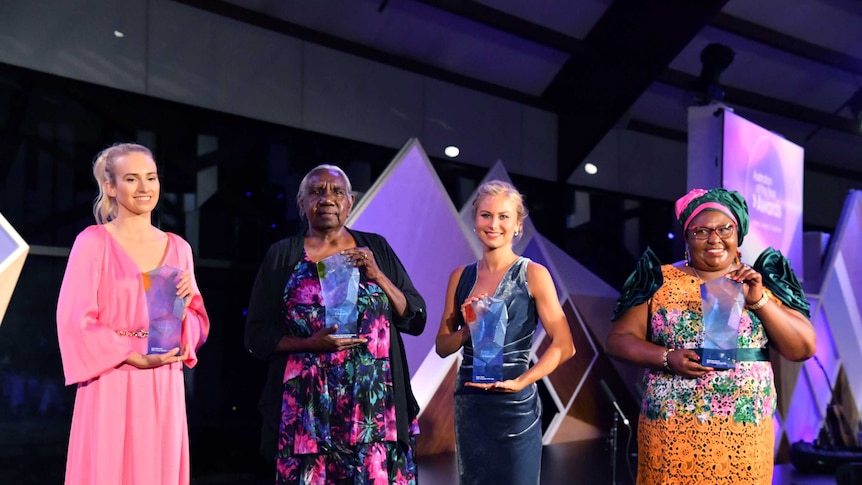 The four women smile, holding their awards on stage.