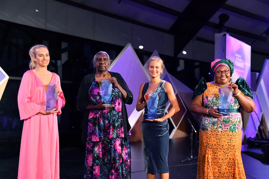 The four women smile, holding their awards on stage.