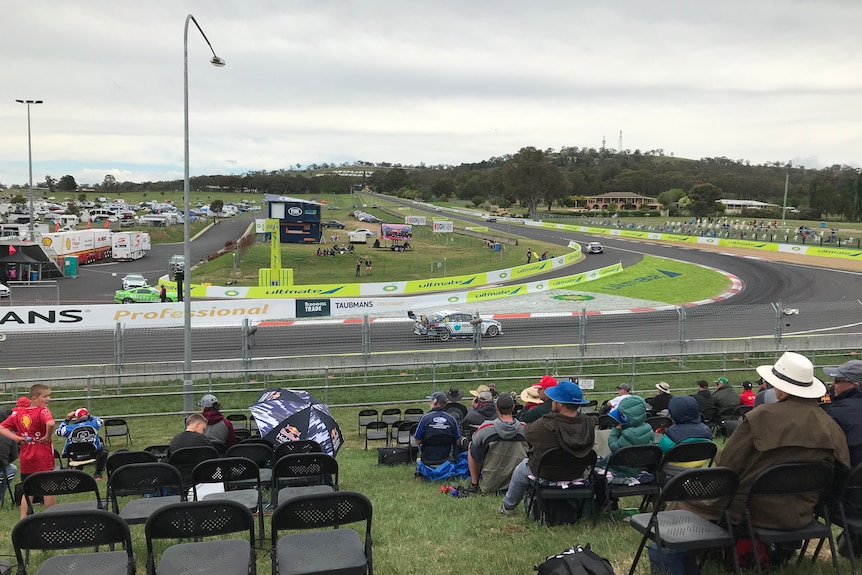 Empty seats in the final corner of Mount Panorama as a white car goes past fans 