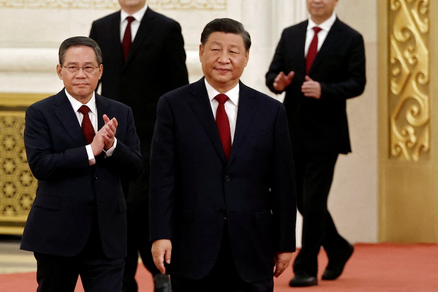 Xi Jinping walks in a suit with political allies clapping behind him.