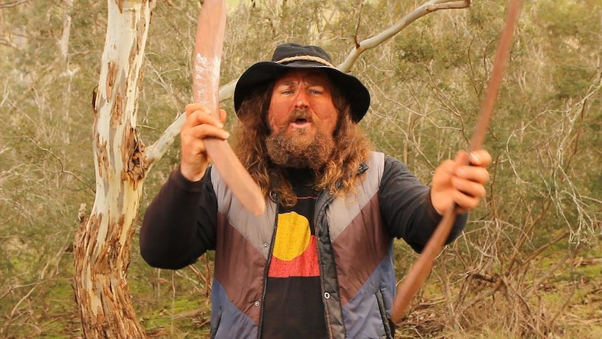 Indigenous man holds boomerang clap sticks