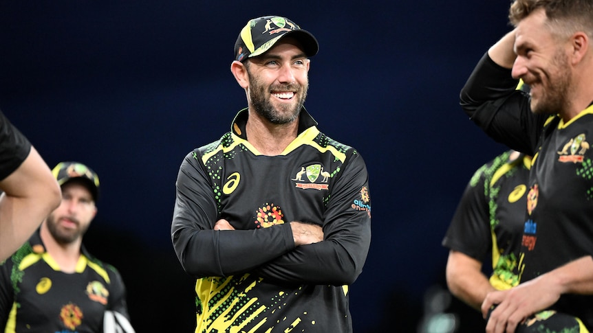 A man with a beard in an Australian T20 cricket uniform smiles and crosses his arms.