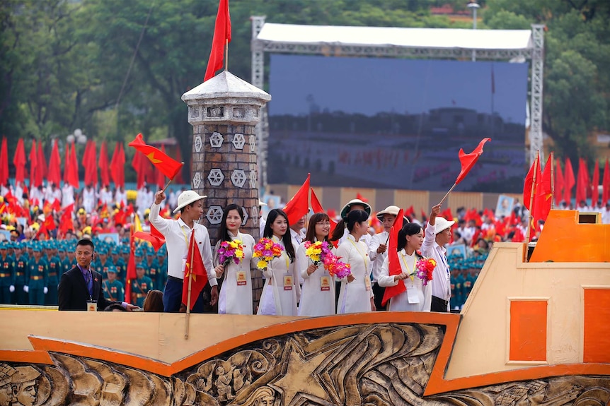Hanoi youth carrying flowers and waving the Vietnamese flags appear on a float in the parade.