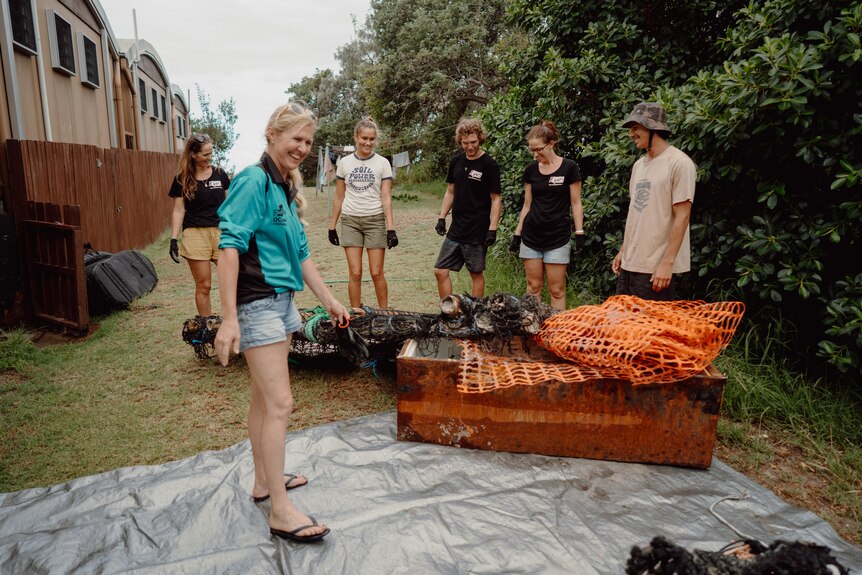 A group of people stand around large pieces of flood debris and rubbish.