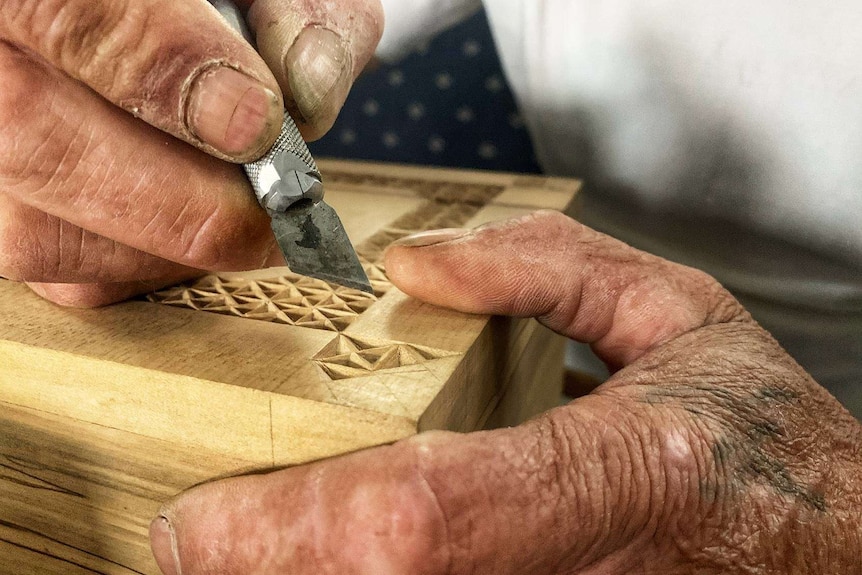 A knife carves a wooden box.
