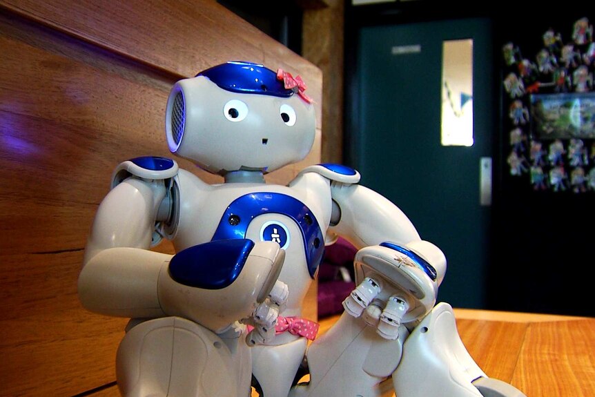 A small, human-like robot sits on a shelf.