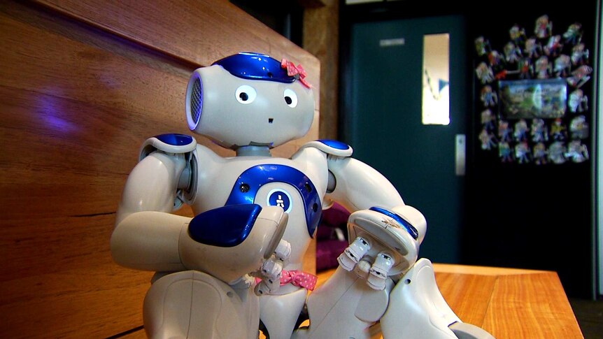 A small, human-like robot sits on a shelf.