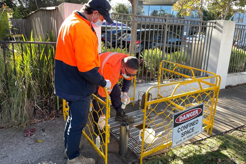 Two men in hi-vis clothes collect waste water.