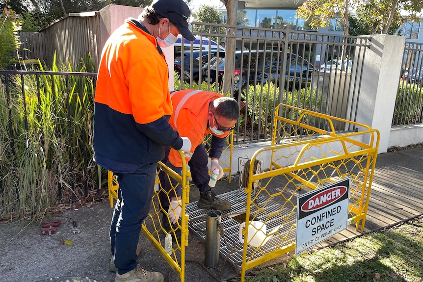 Two men in hi-vis clothes collect waste water.