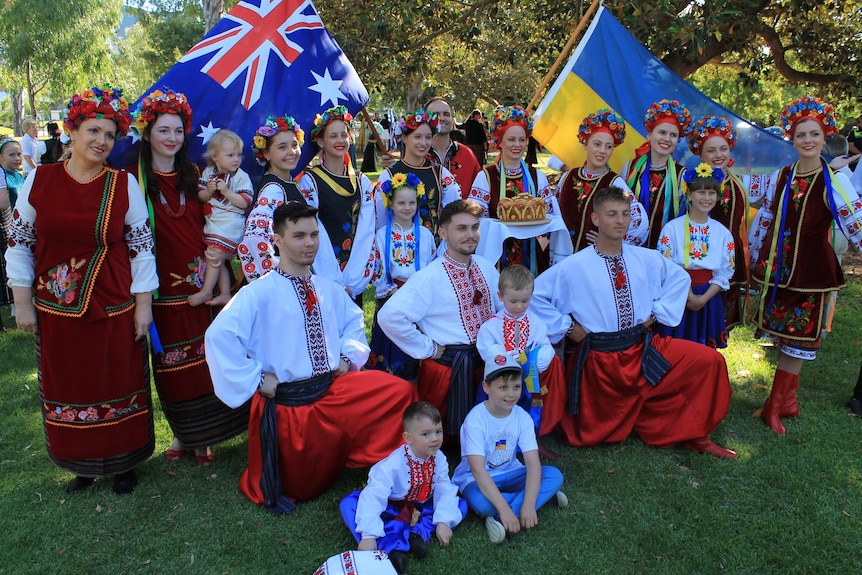 A group of men and women in traditional Ukrainian costume pose for a photograph with Australian and Ukrainian flags.
