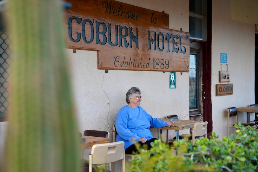 An elderly white woman wearing a blue skivvy sitting on the verandah of the coburn hotel