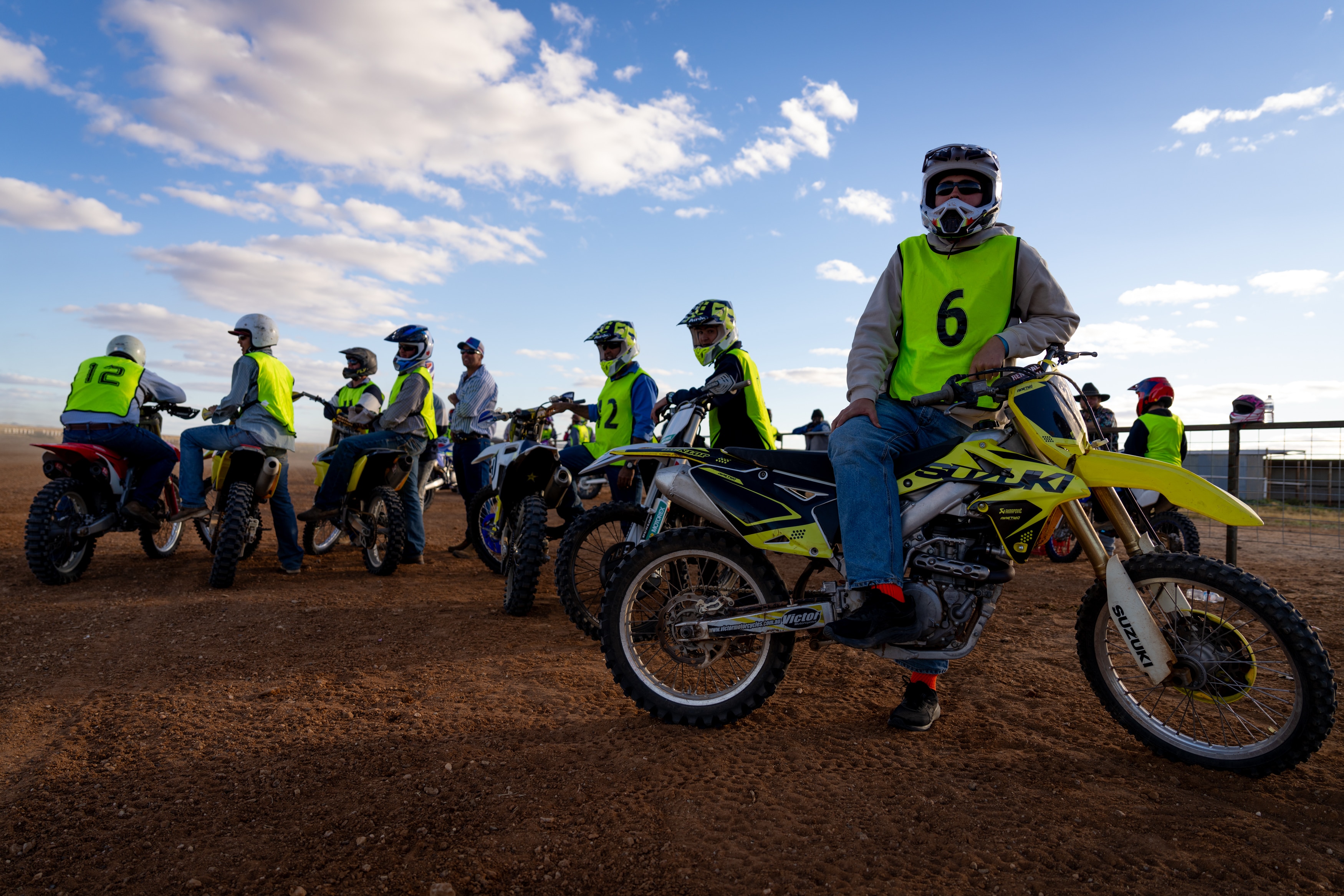 A man on a motorbike looking at the camera, with a group of people on motorbikes in the background