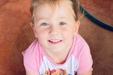 A close-up shot of a smiling Cleo Smith sitting on the floor looking up at the camera.