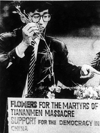 You view a black and white image of a young Chinese man laying flowers behind a memorial sign for the Tiananmen Square massacre.