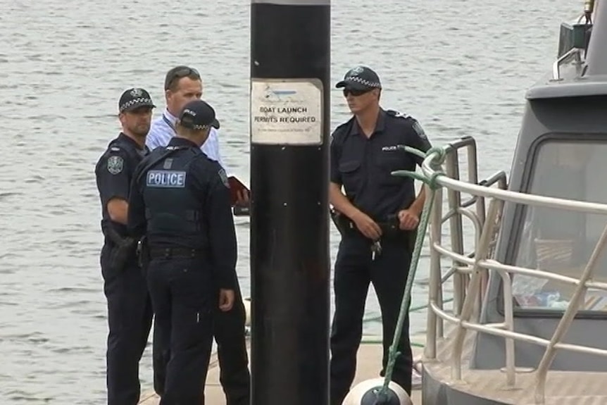 Three police officers and a detective standing around a boat