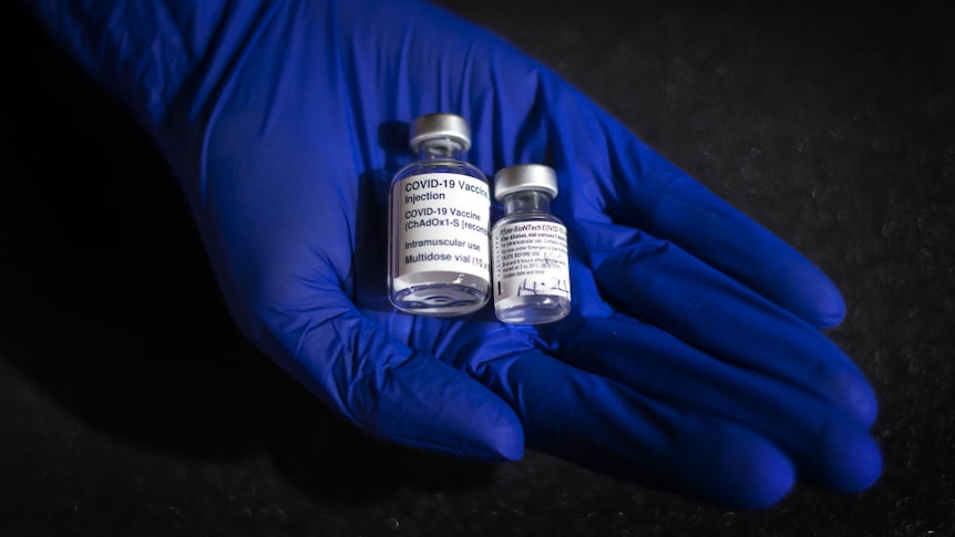 A blue glove holds two covid vaccine bottles.