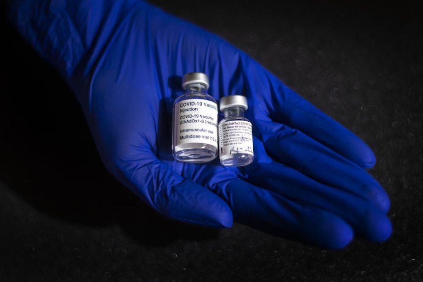 A blue glove holds two covid vaccine bottles.