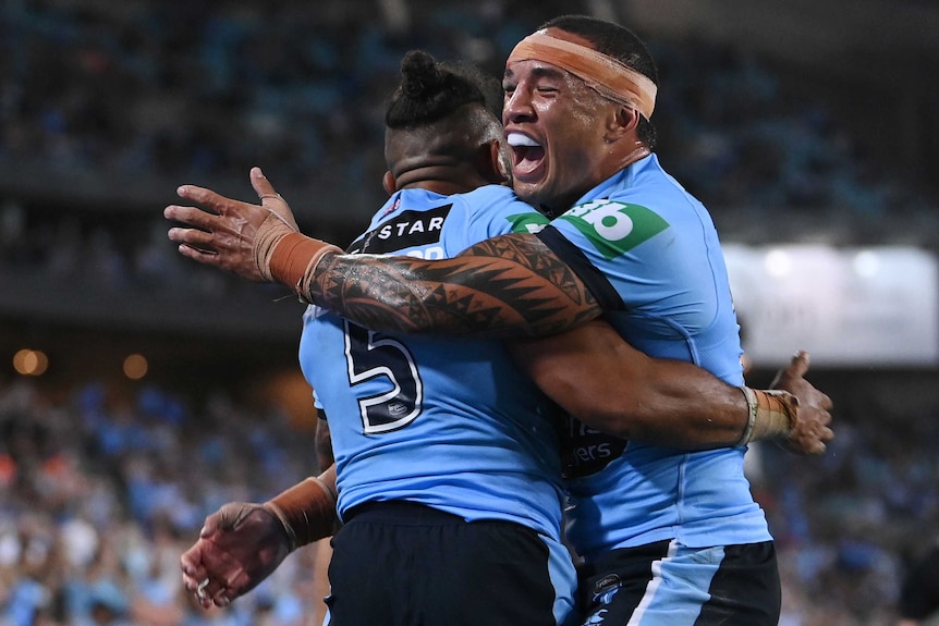 Two male New South Wales State of Origin players embrace as they celebrate a try against Queensland.