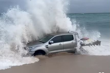 Silver ute on the beach with a wave crashing over it