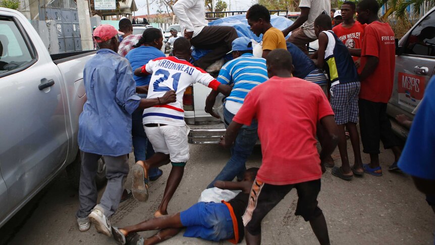 A boy falls to the ground with a looted bag of donated goods, as men snatch other bags from a truck in Haiti, October 16 2016.
