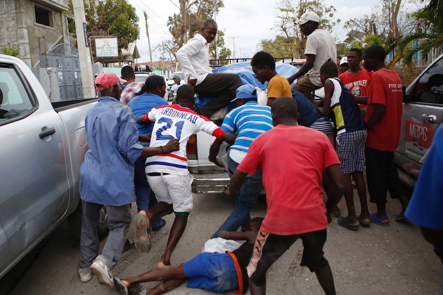 A boy falls to the ground with a looted bag of donated goods, as men snatch other bags from a truck in Haiti, October 16 2016.