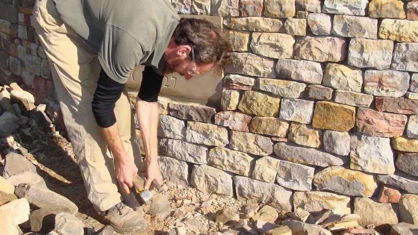 Andrew Garner bends and hammers a piece of sandstone