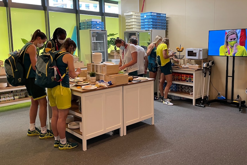 Australian Olympic athletes stand at tables and make food in a makeshift kitchen at the Tokyo Olympics.