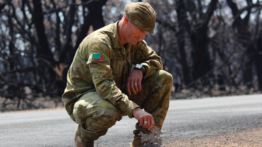 An army reservist kneels by a roadside.