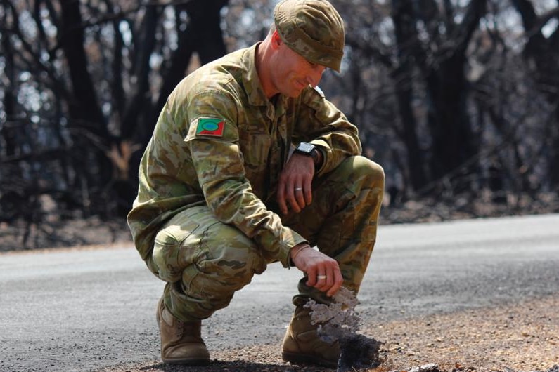 An army reservist kneels by a roadside.