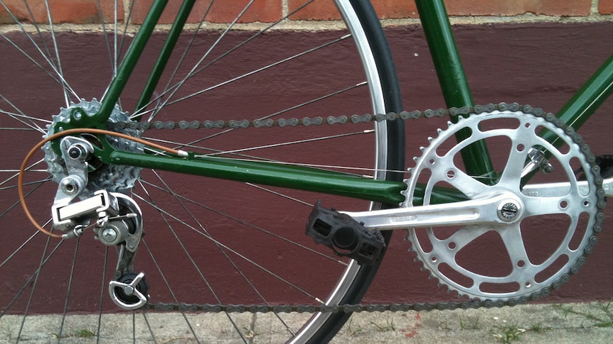 The back wheel of a green bicycle leaning against a dark red brick wall.