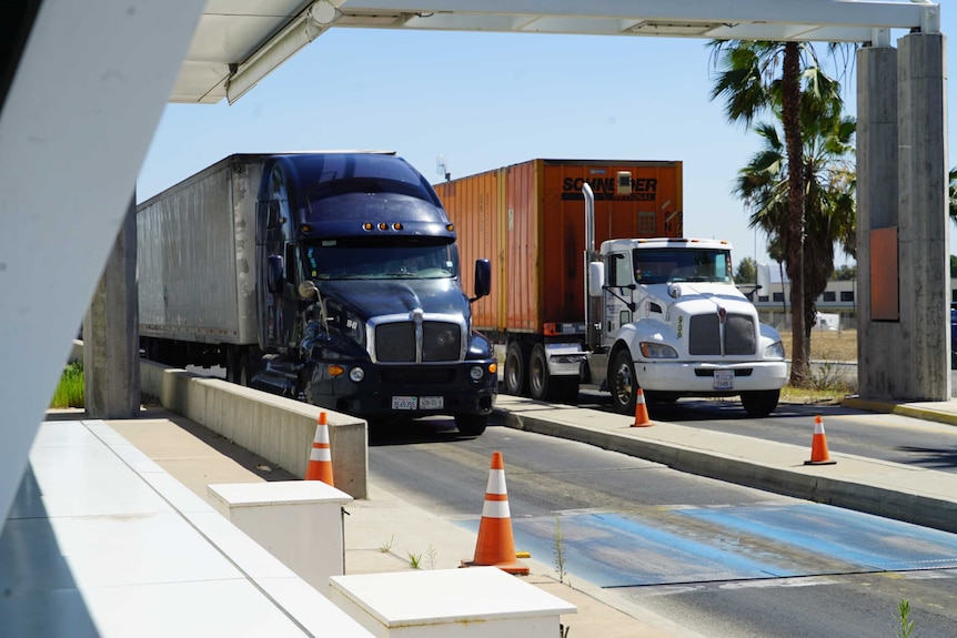 Two semi-trailer trucks are stopped at a border crossing