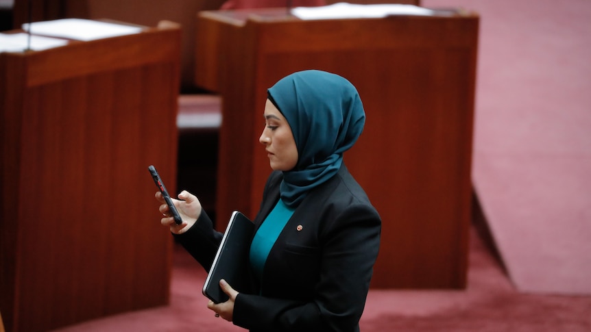 A woman wearing a hijab looks at her phone.